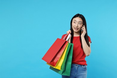 Photo of Smiling woman with shopping bags talking by smartphone on light blue background. Space for text