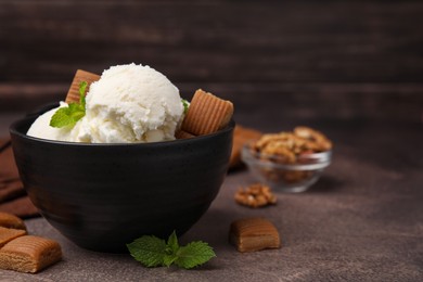 Photo of Tasty ice cream with caramel candies and mint in bowl on brown table, closeup. Space for text