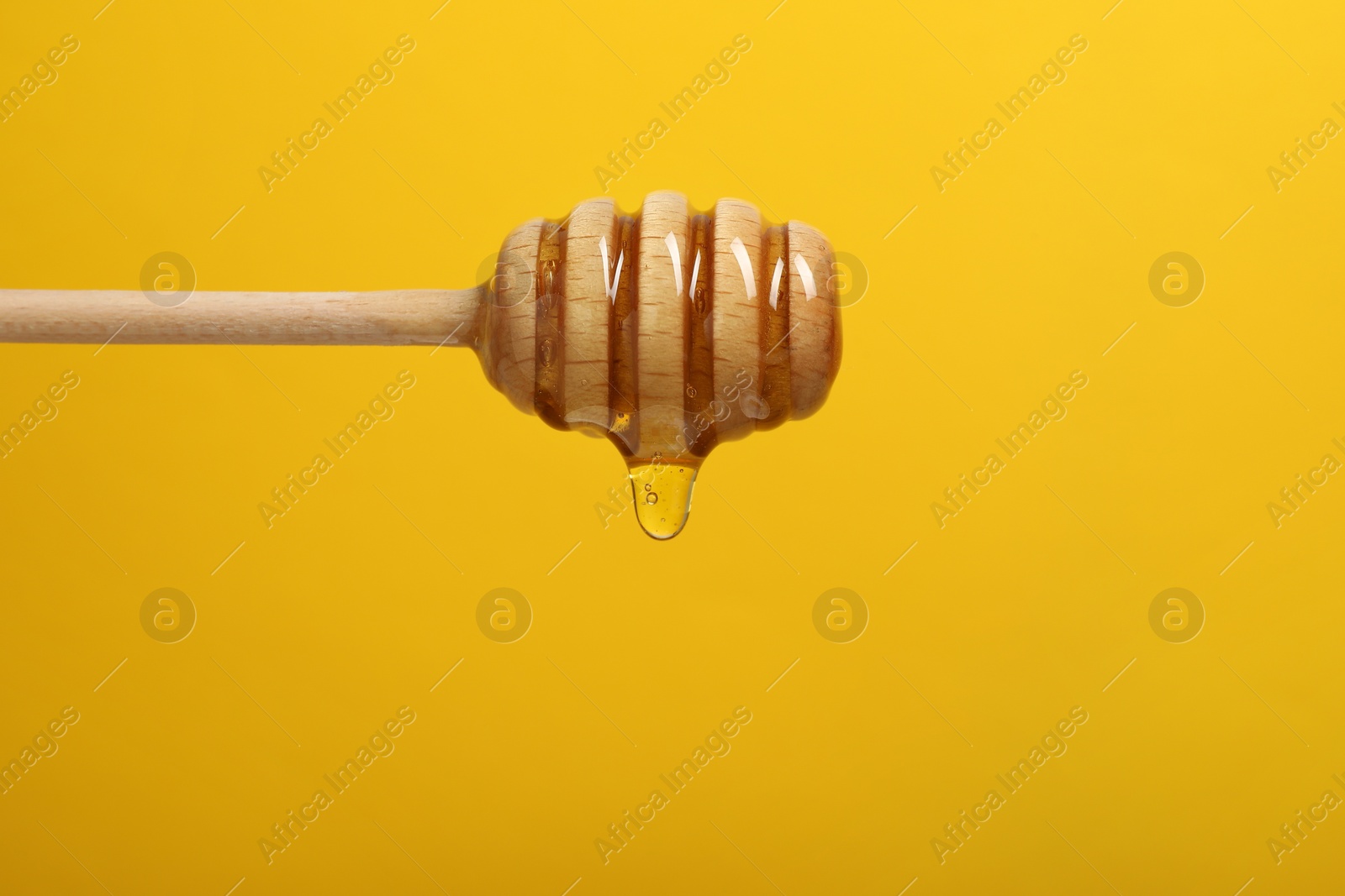 Photo of Pouring honey from dipper against yellow background, closeup. Space for text