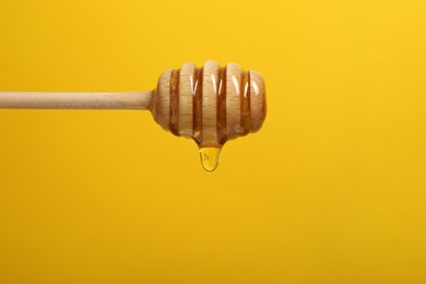 Photo of Pouring honey from dipper against yellow background, closeup. Space for text