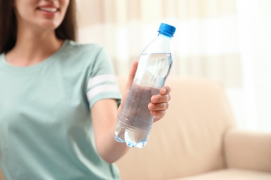 Woman with bottle of fresh water indoors, closeup