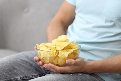 Photo of Man with bowl of potato chips on grey sofa, closeup