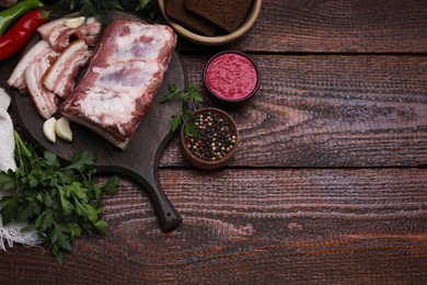 Photo of Pieces of pork fatback served with sauce and spices on wooden table, flat lay. Space for text