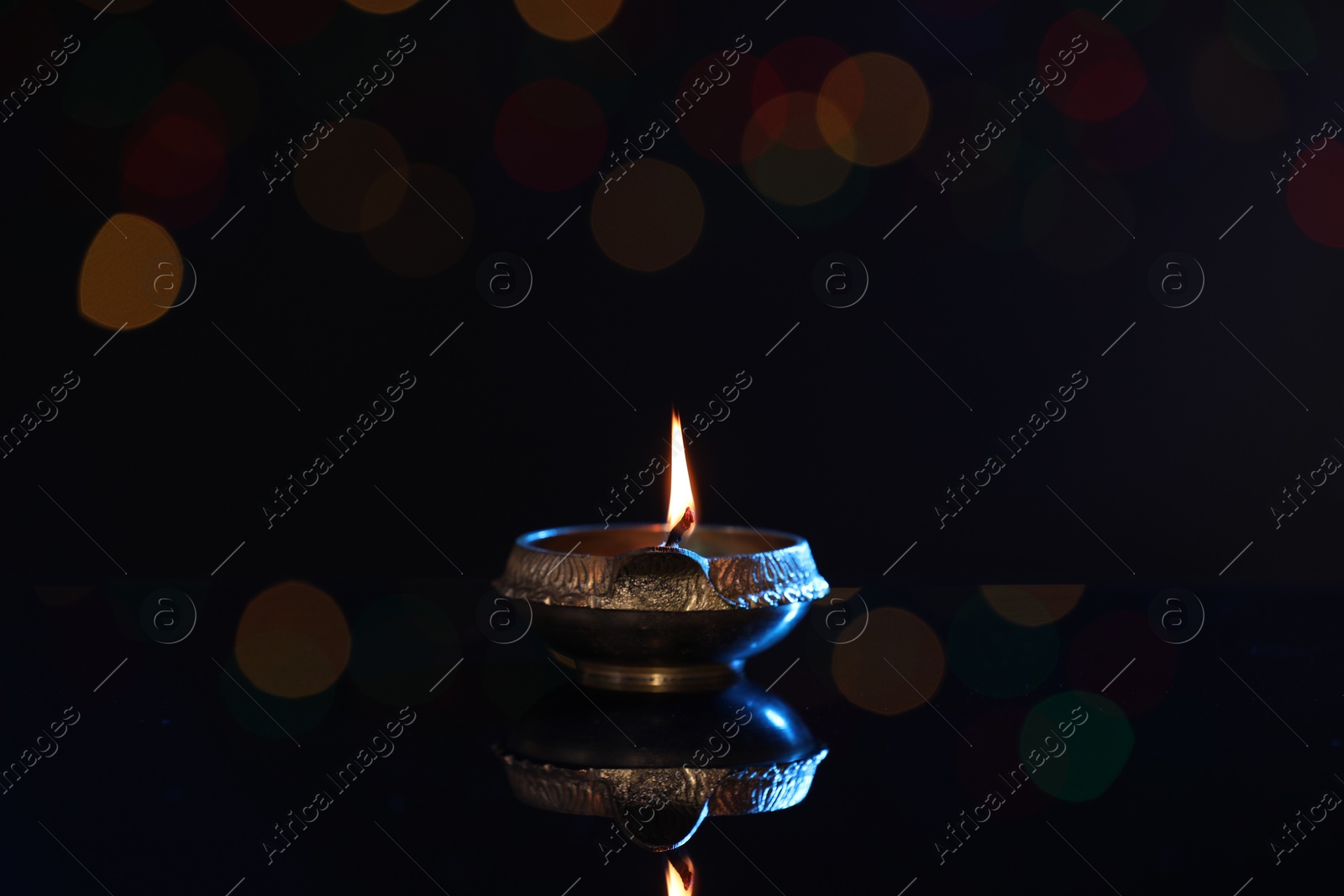 Photo of Lit diya on dark background with blurred lights, space for text. Diwali lamp