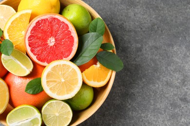 Different fresh citrus fruits and leaves in bowl on grey textured table, top view. Space for text