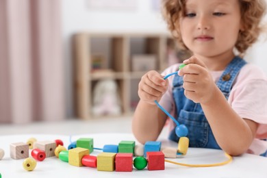 Photo of Motor skills development. Little girl playing with wooden pieces and string for threading activity at table indoors, closeup