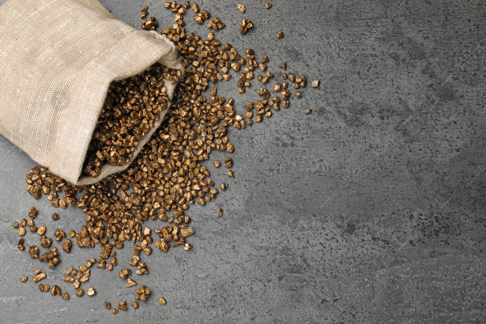 Photo of Overturned sack of gold nuggets on grey table, flat lay. Space for text