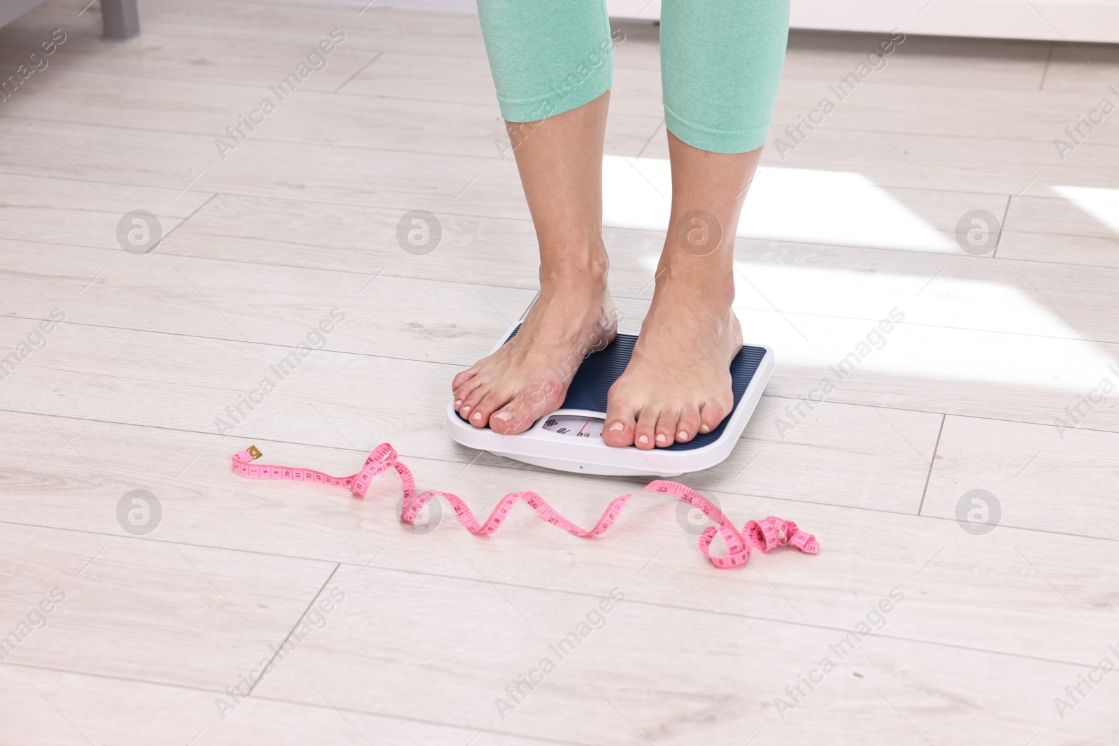 Photo of Woman on floor scale and measuring tape at home, closeup. Weight control