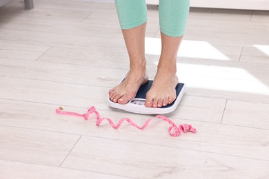 Photo of Woman on floor scale and measuring tape at home, closeup. Weight control