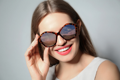 Image of Young woman wearing stylish sunglasses with reflection of sky on light grey background