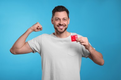 Happy man holding condom on light blue background