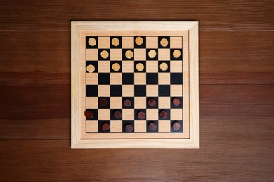 Photo of Checkerboard with game pieces on wooden table, top view