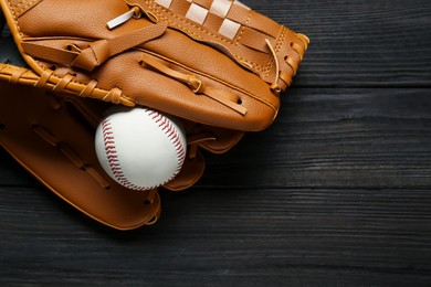 Photo of Catcher's mitt and baseball ball on black wooden table, top view with space for text. Sports game