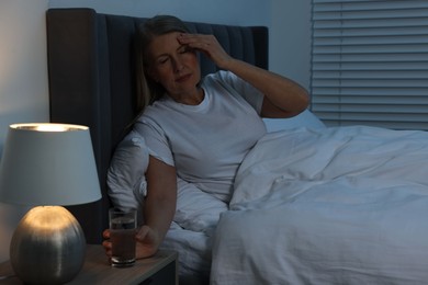 Woman with glass of water suffering from headache in bed at night