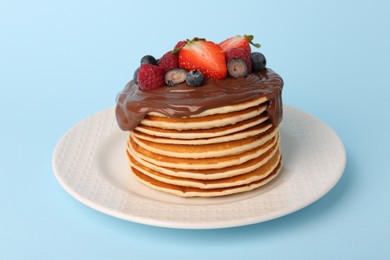 Photo of Stack of tasty pancakes with fresh berries and chocolate spread on light blue background