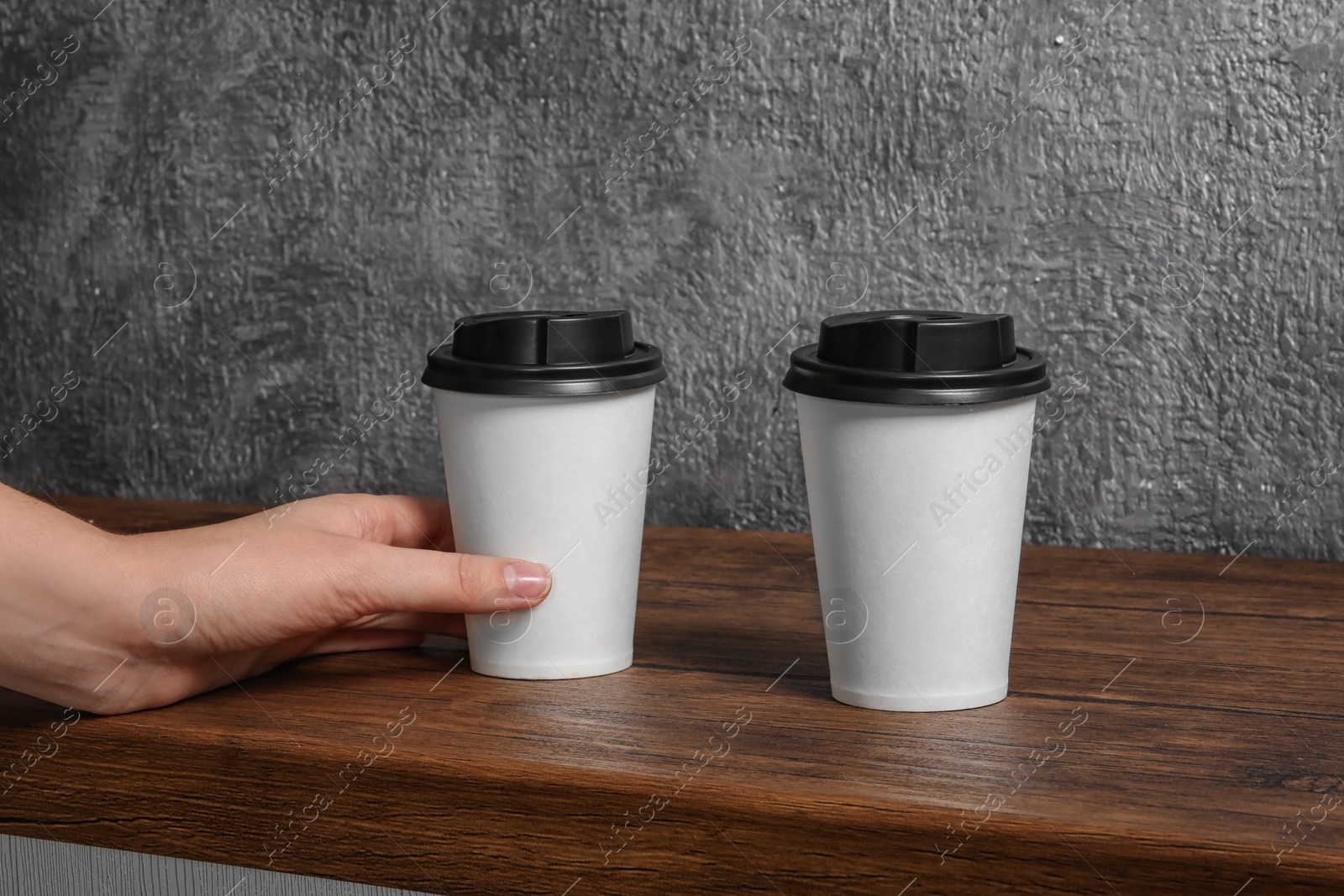 Photo of Woman taking cardboard coffee cup from wooden table