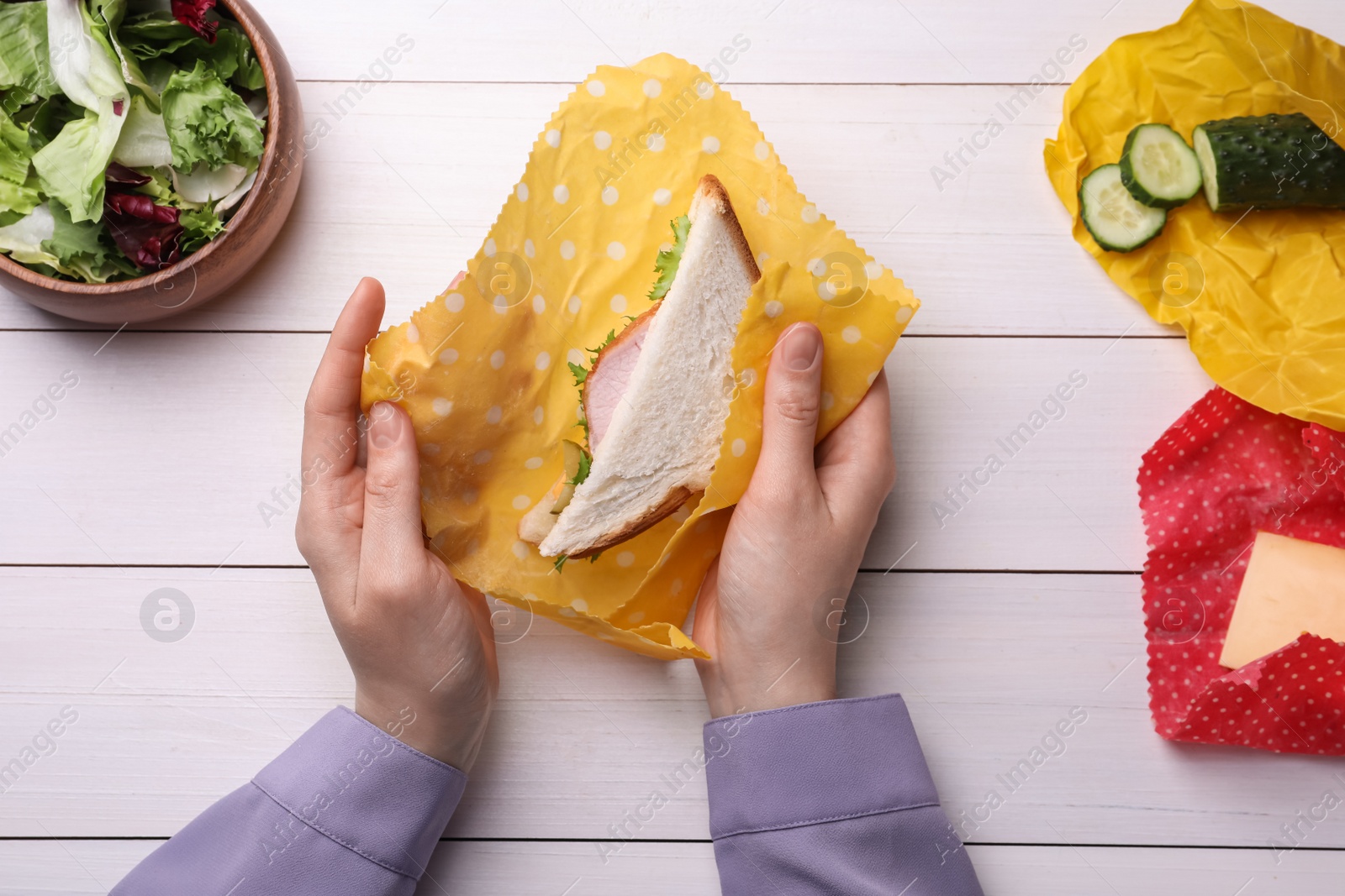 Photo of Woman packing sandwich into beeswax food wrap at white wooden table, top view