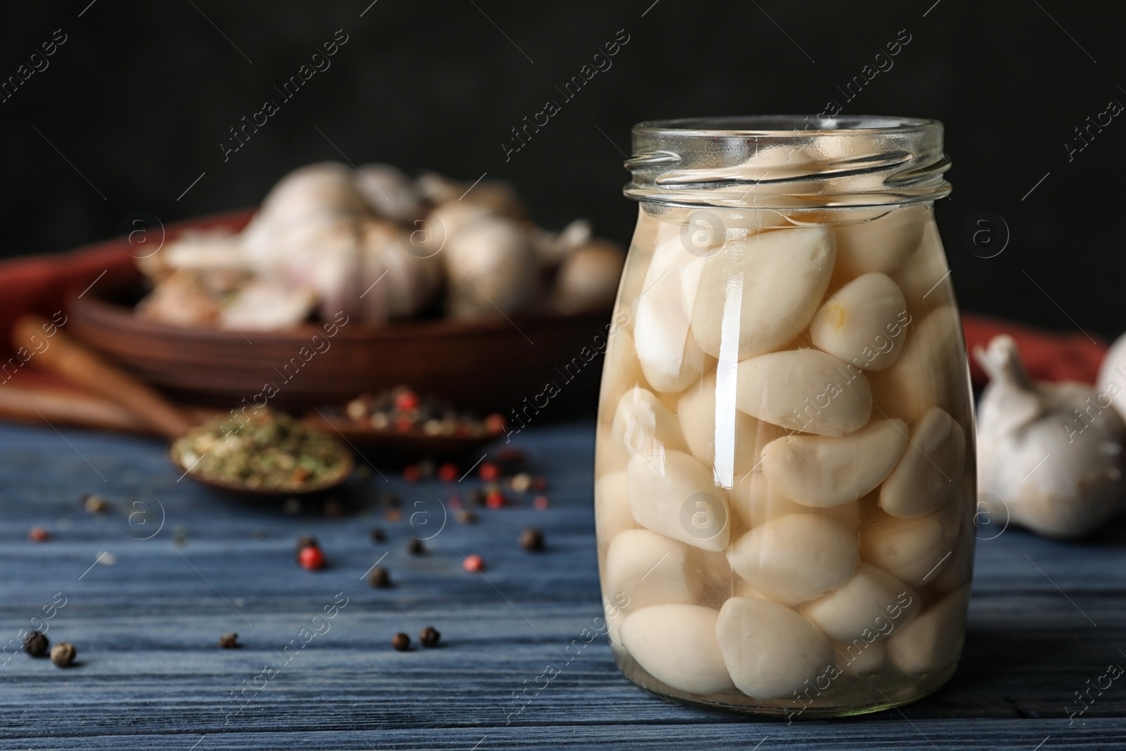 Photo of Preserved garlic in glass jar on wooden table. Space for text