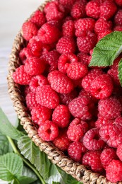 Photo of Tasty ripe raspberries and leaves in wicker basket on table, closeup