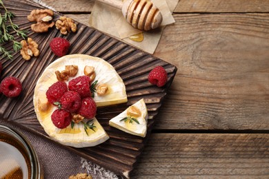 Photo of Brie cheese served with raspberries, walnuts and honey on wooden table, flat lay. Space for text