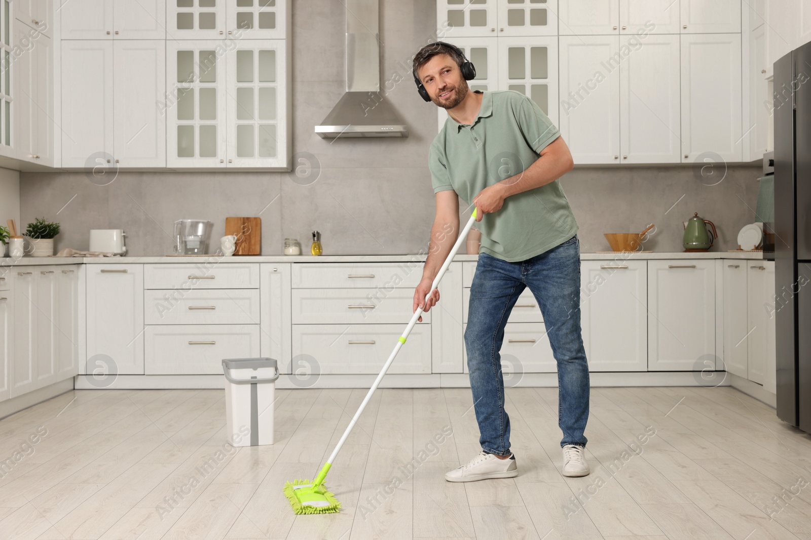 Photo of Enjoying cleaning. Man in headphones listening to music and mopping floor in kitchen