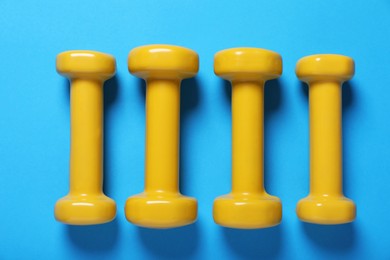 Photo of Yellow dumbbells on light blue background, flat lay. Morning exercise