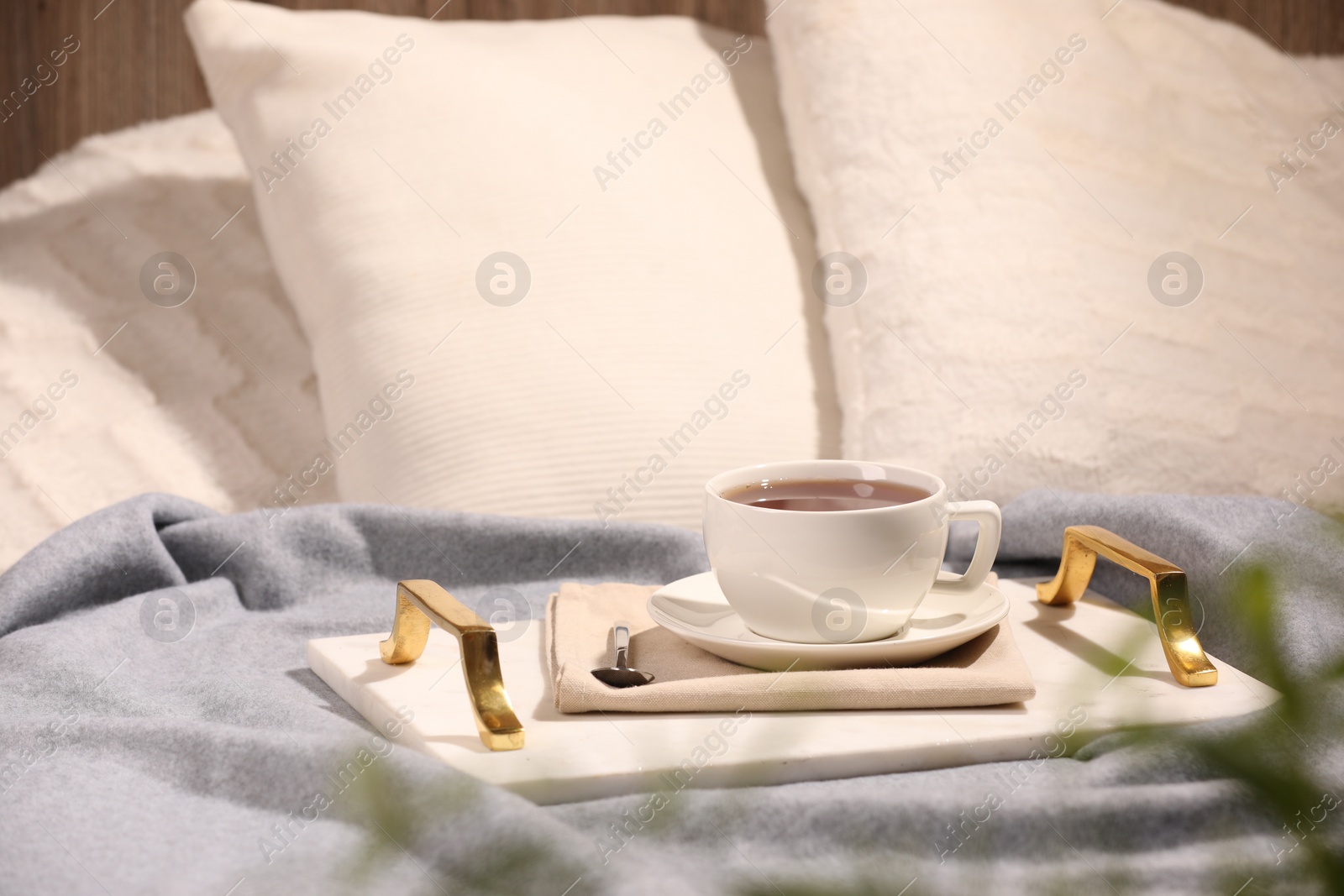 Photo of Aromatic tea in cup, saucer and spoon on bed
