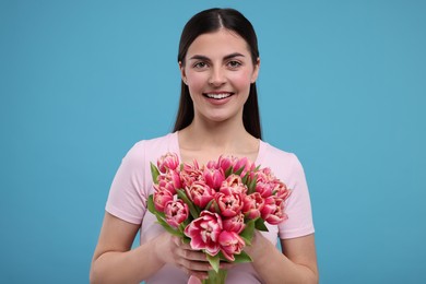 Photo of Happy young woman with beautiful bouquet on light blue background