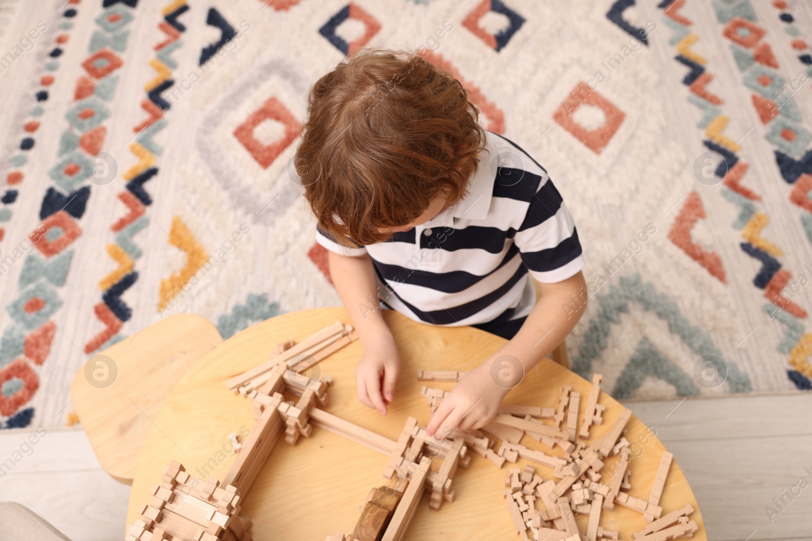 Photo of Little boy playing with wooden entry gate at table in room. Child's toy