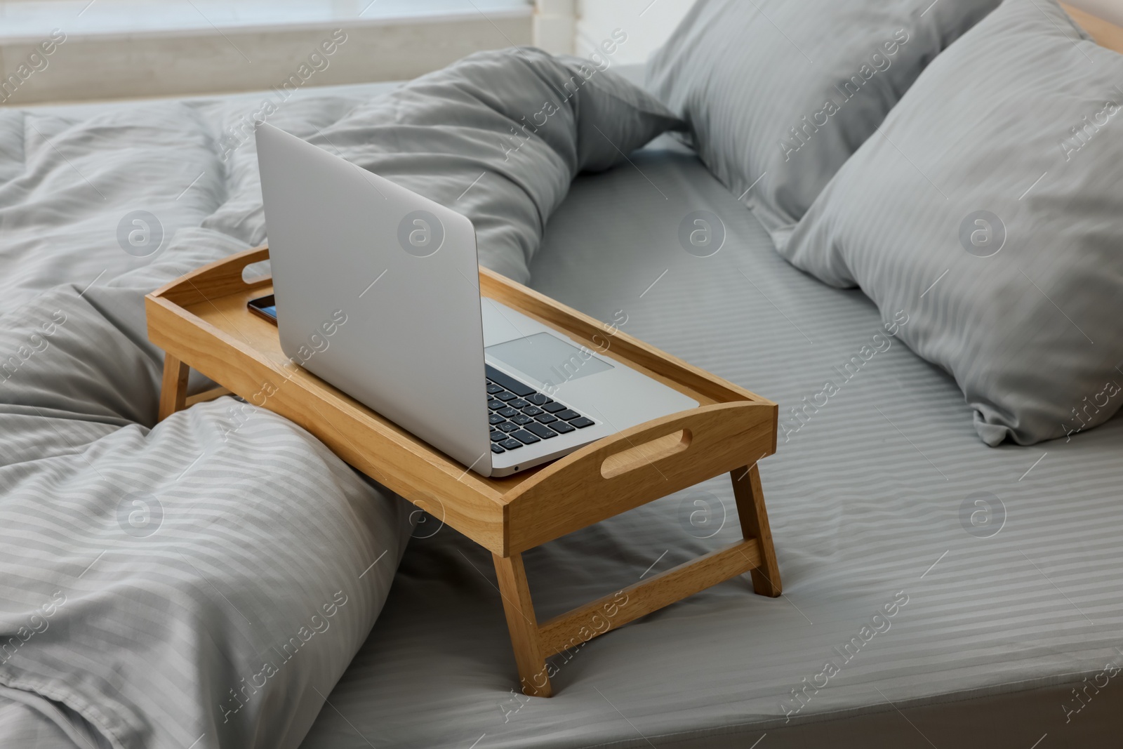 Photo of Wooden tray table with laptop on bed indoors