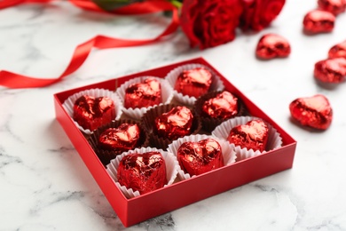 Box with heart shaped chocolate candies on white marble table