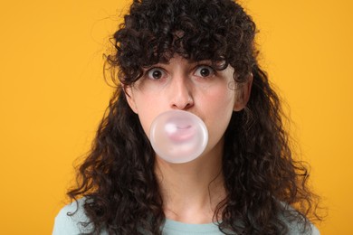 Photo of Beautiful young woman blowing bubble gum on orange background