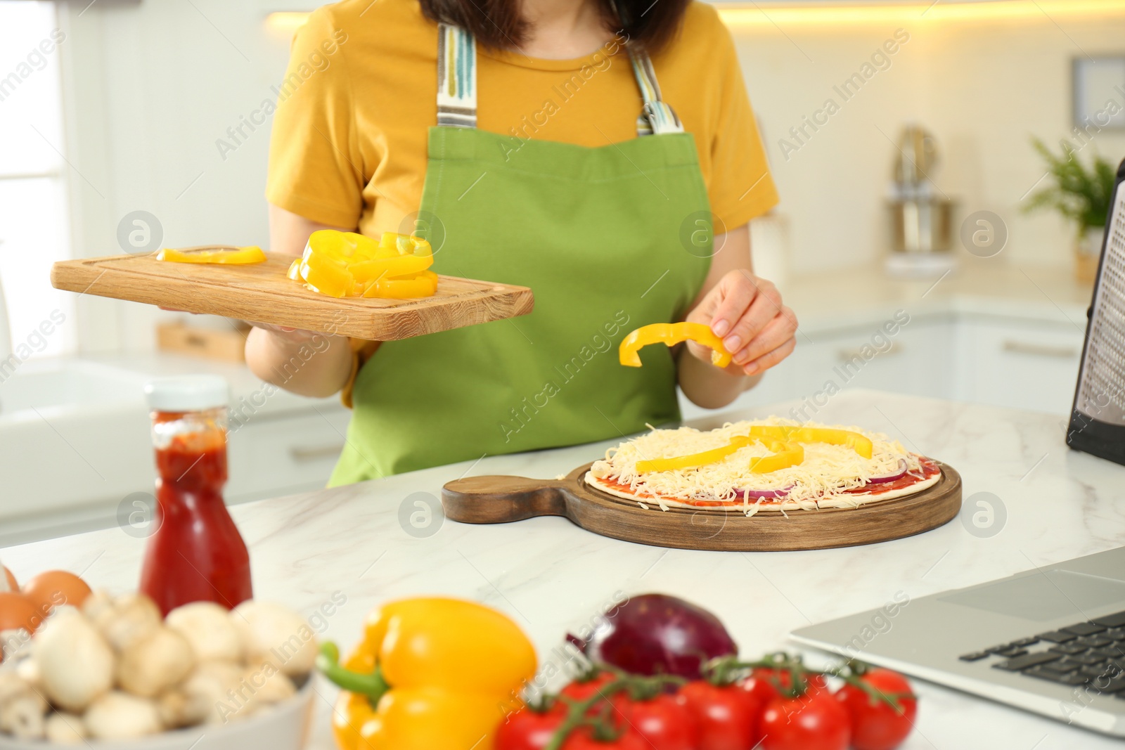 Photo of Woman making pizza while watching online cooking course via laptop in kitchen, closeup