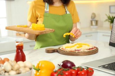 Woman making pizza while watching online cooking course via laptop in kitchen, closeup