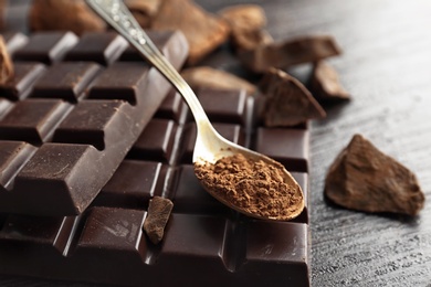 Photo of Spoon with cocoa powder and tasty chocolate on dark table, closeup