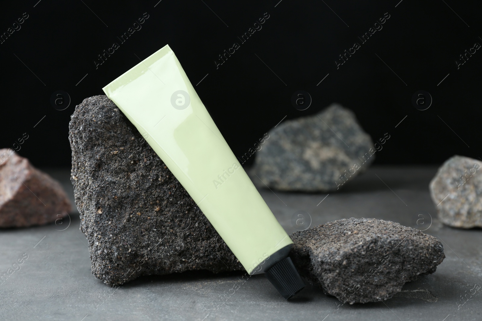 Photo of Tube of hand cream among stones on grey table against dark background. Mockup for design