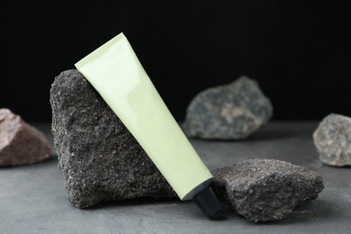 Photo of Tube of hand cream among stones on grey table against dark background. Mockup for design