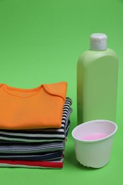 Photo of Stack of baby clothes and laundry detergents on light green background