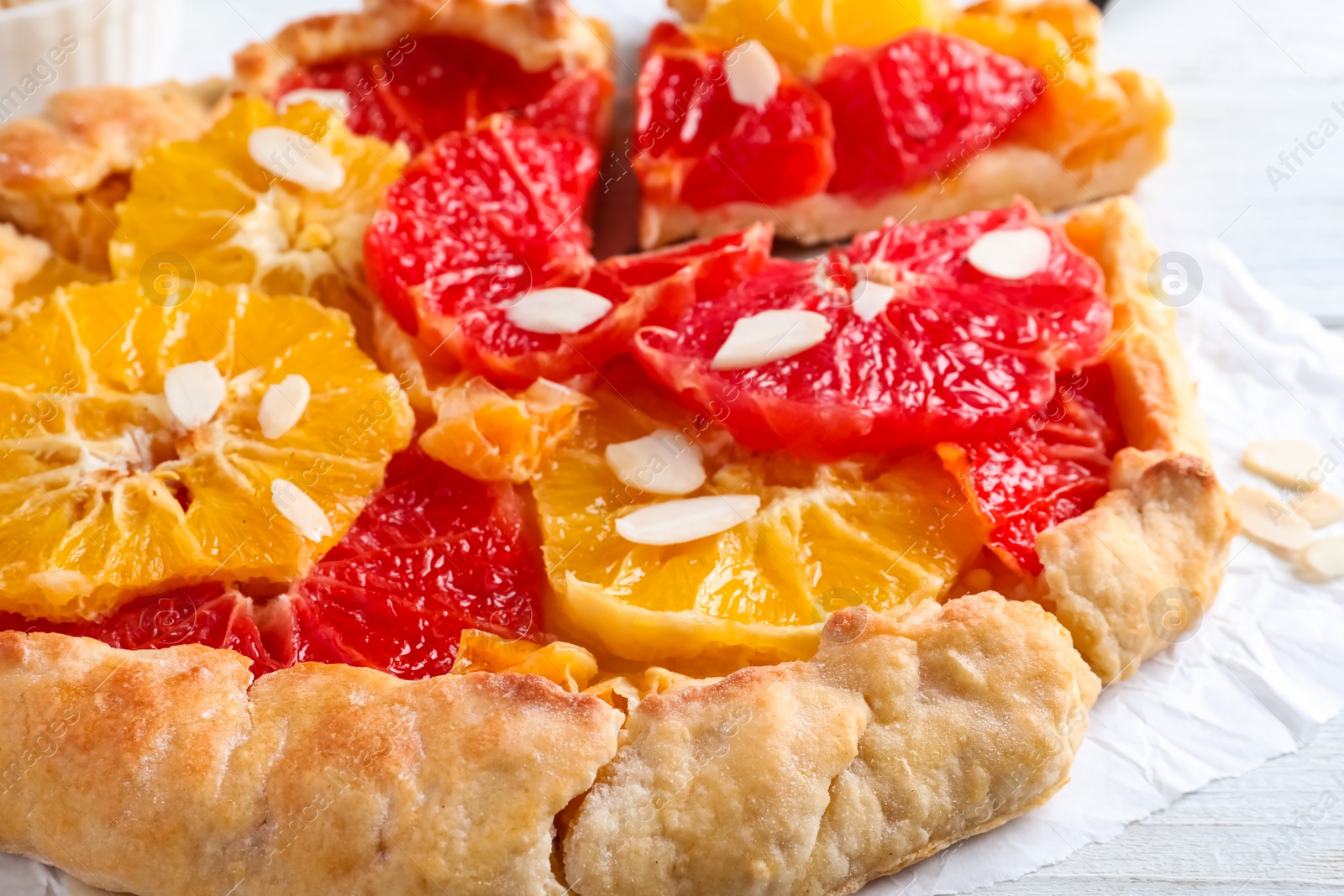 Photo of Tasty galette with citrus fruits and almond flakes on table, closeup