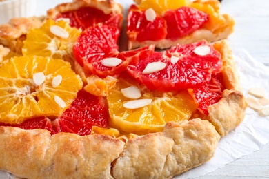 Photo of Tasty galette with citrus fruits and almond flakes on table, closeup