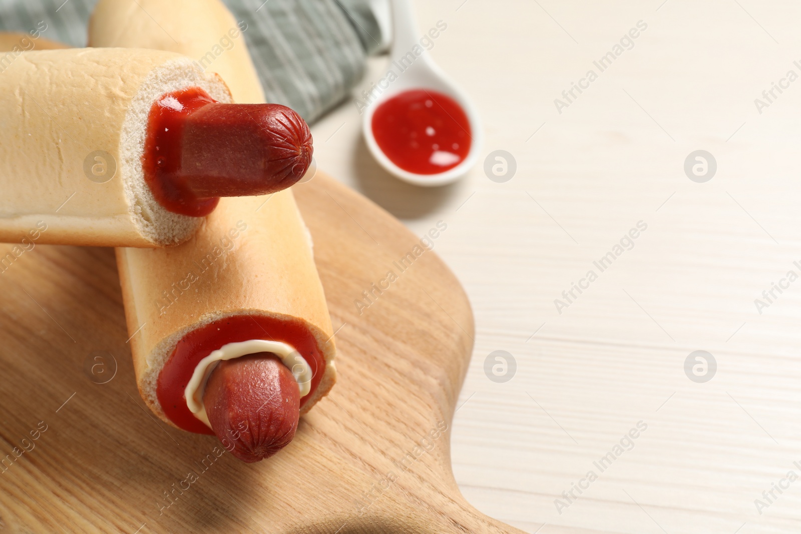 Photo of Tasty french hot dogs and dip sauce on white wooden table, closeup. Space for text
