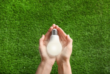 Image of Woman holding glowing light bulb over green grass, top view