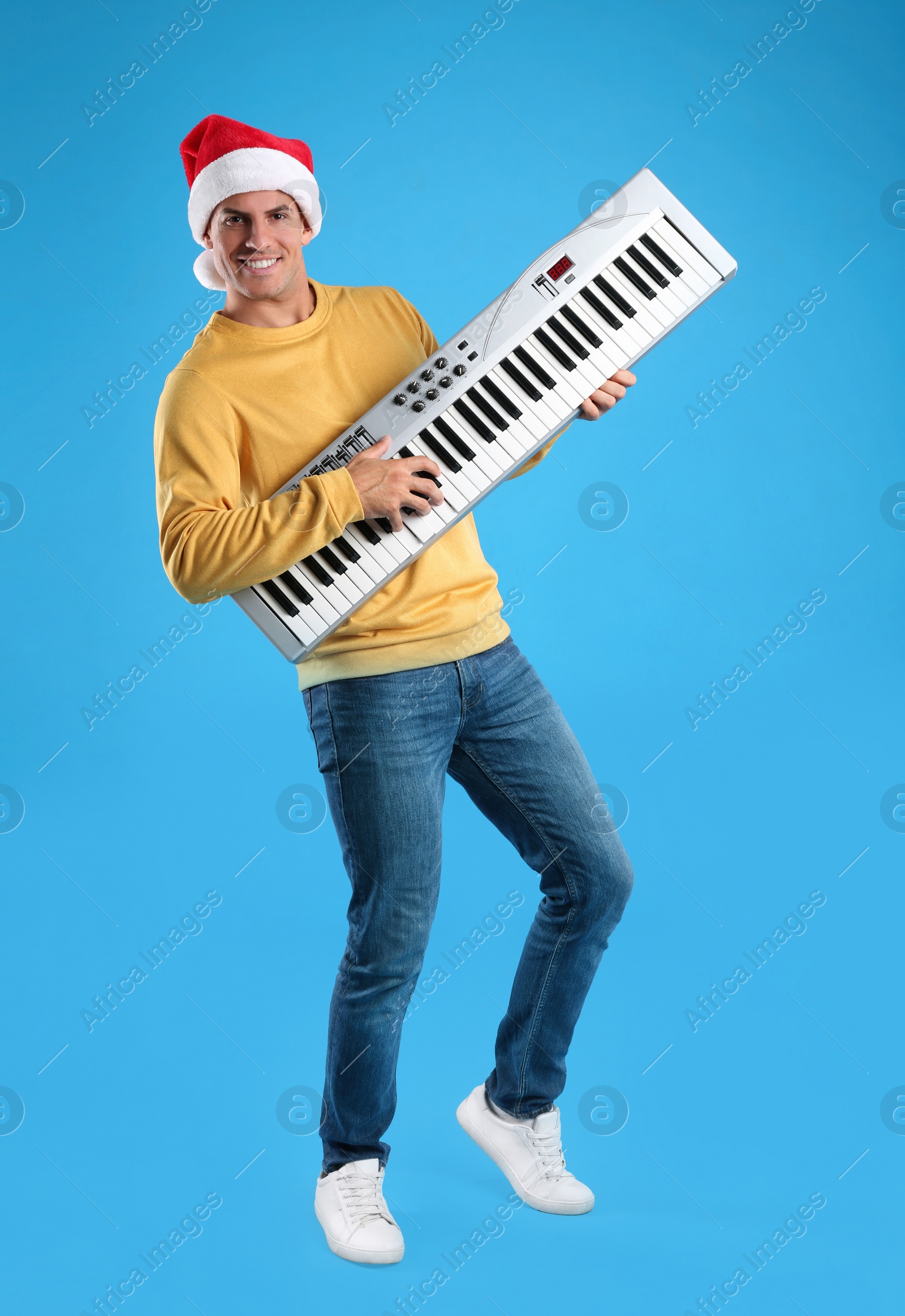 Photo of Man in Santa hat playing synthesizer on light blue background. Christmas music