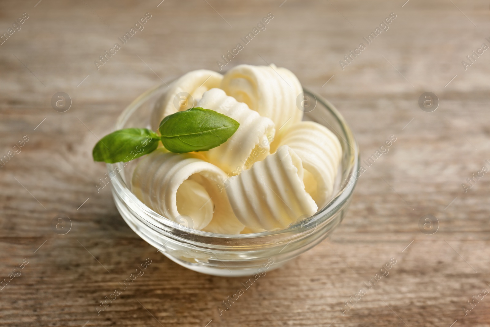 Photo of Bowl with tasty butter curls on wooden background