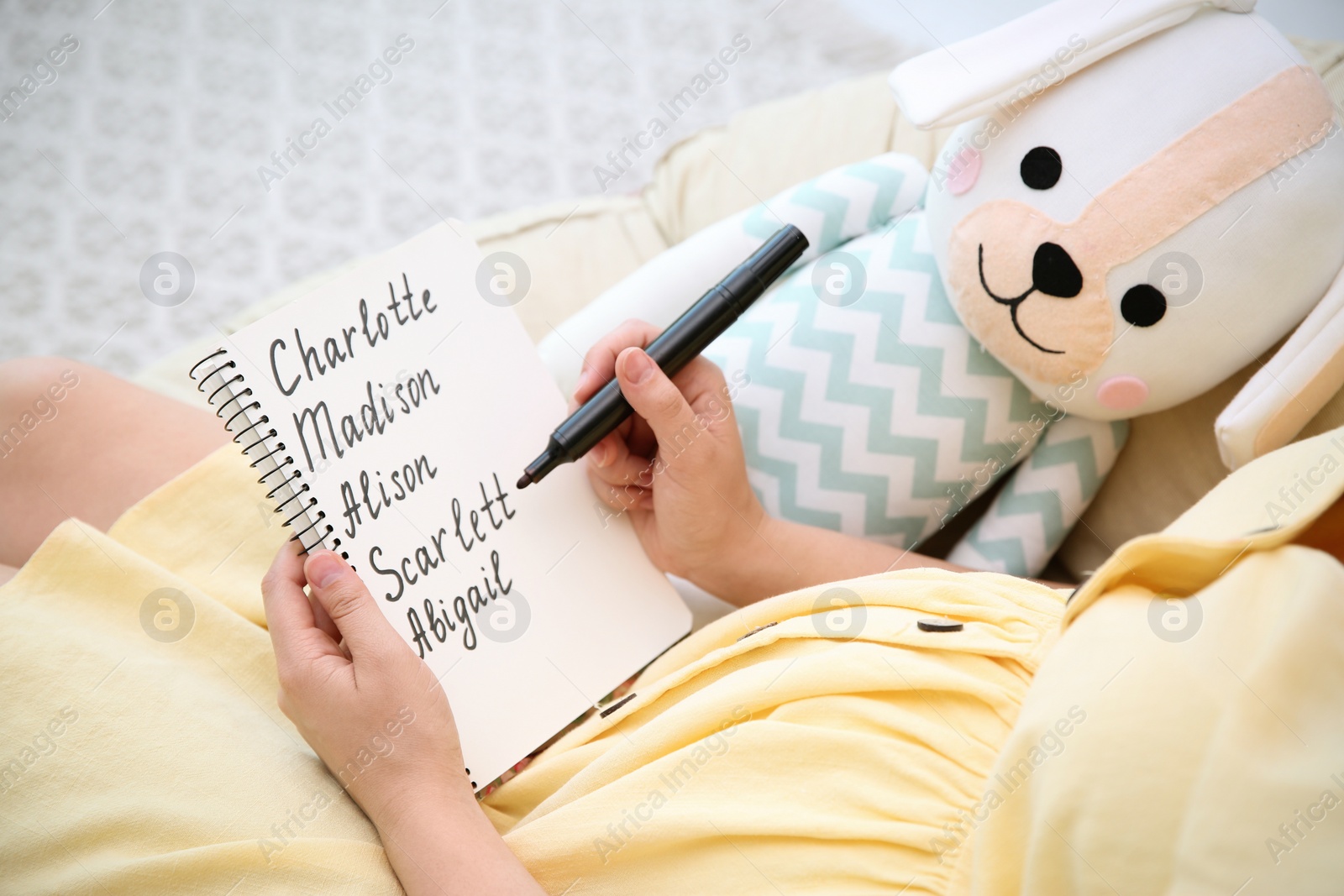 Photo of Pregnant woman with baby names list sitting in armchair, closeup