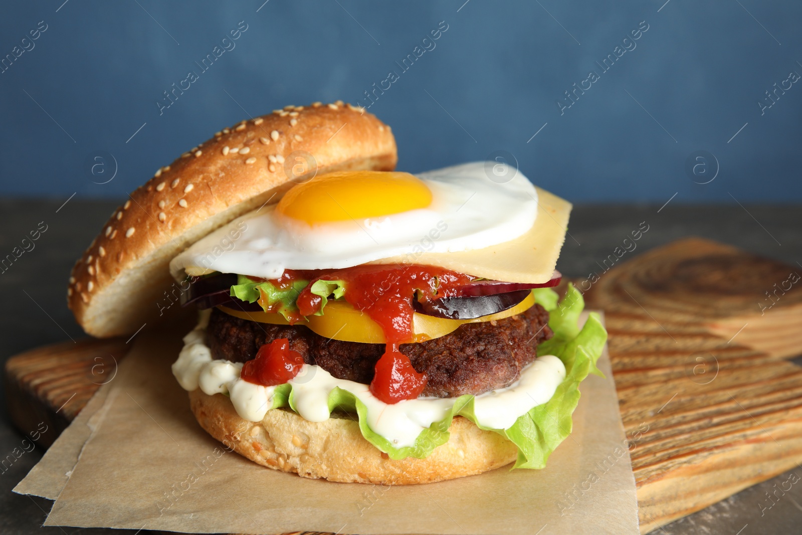 Photo of Tasty burger with fried egg on board against color background