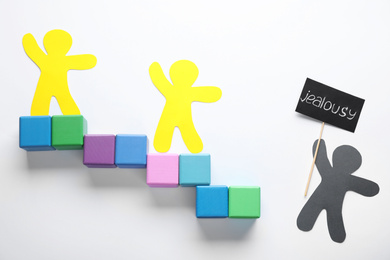 Photo of Human paper figures and stairs made of cubes on white background, flat lay. Concept of jealousy