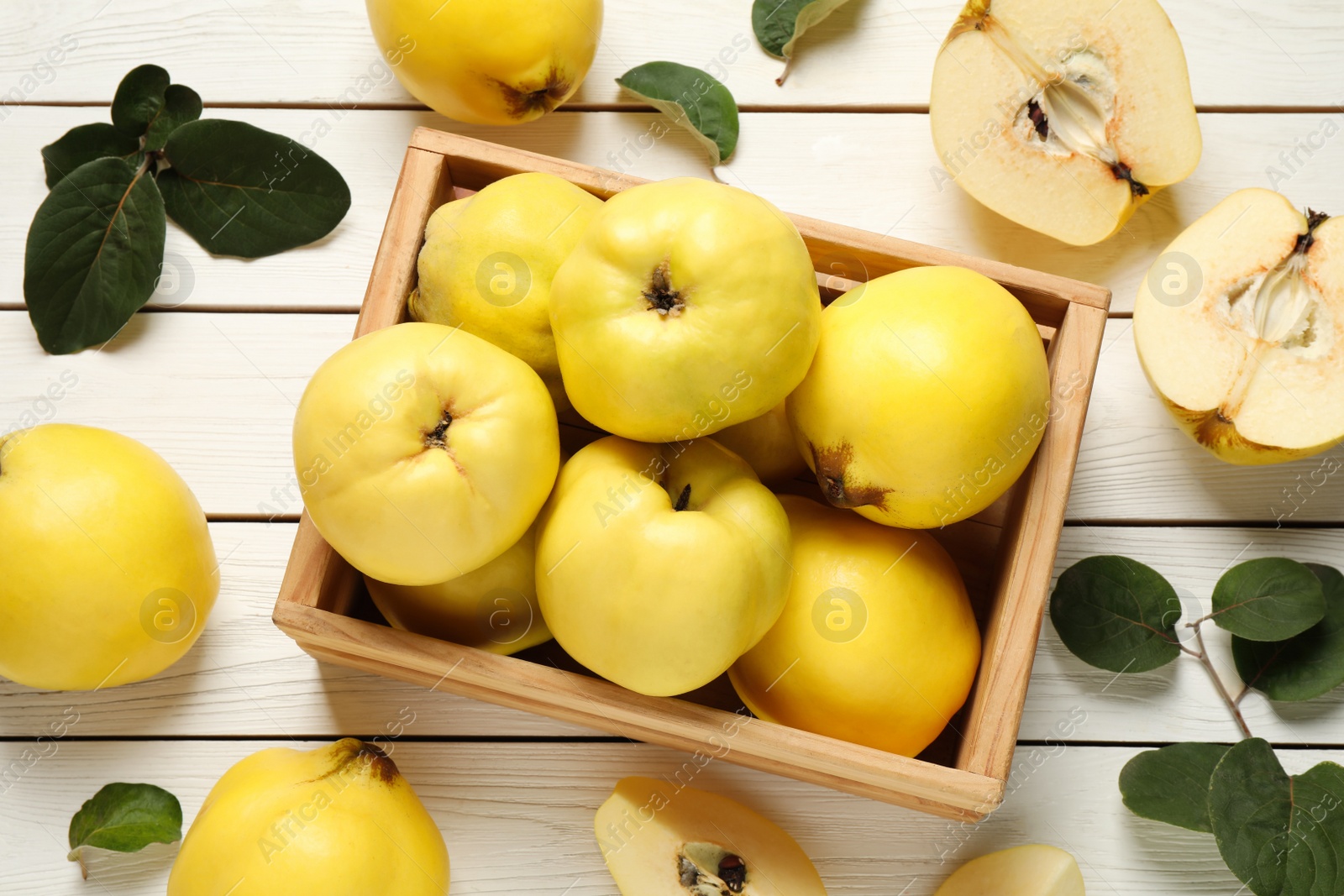 Photo of Fresh ripe organic quinces and leaves on white wooden table, flat lay