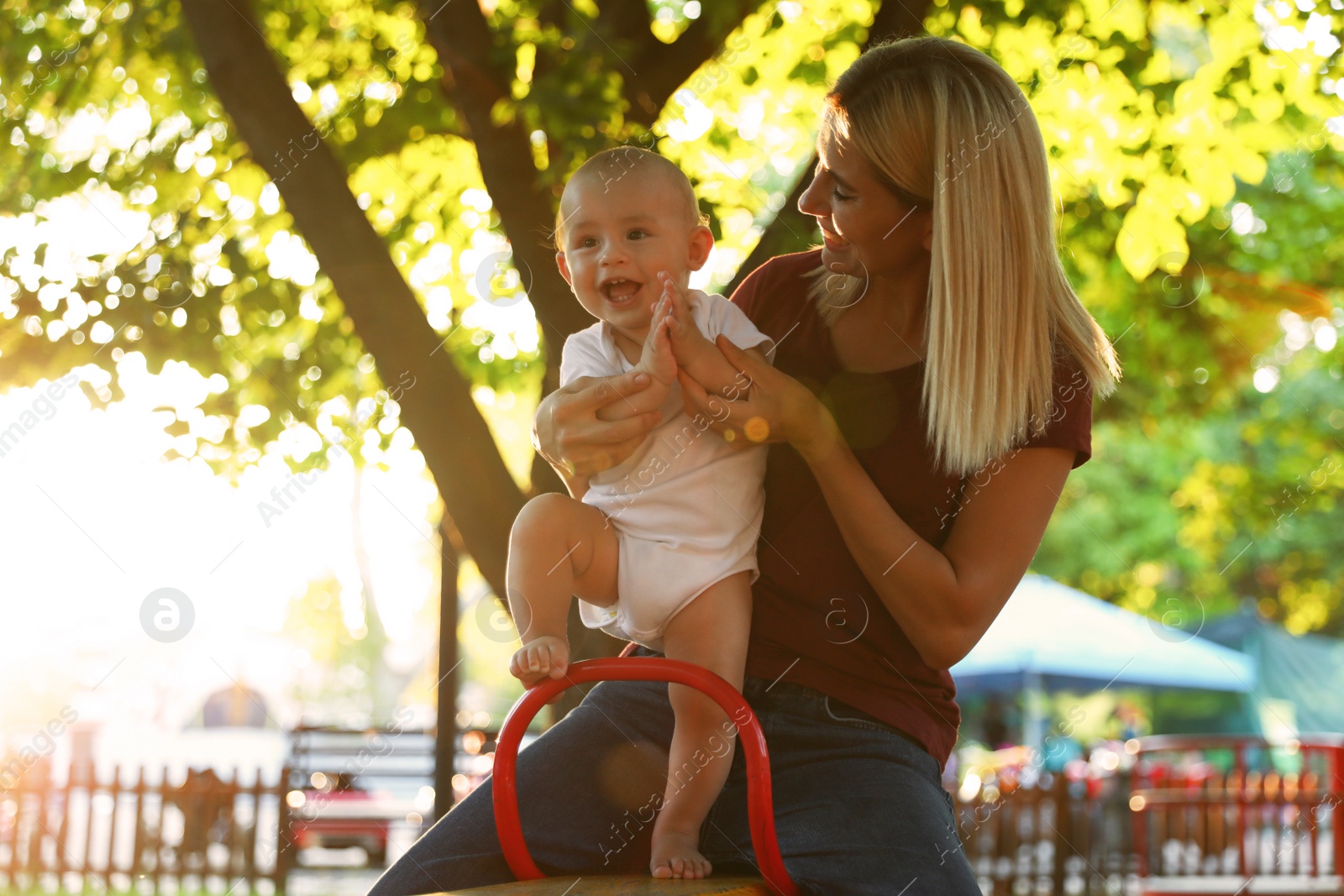 Photo of Nanny and cute baby sitting on seesaw outdoors