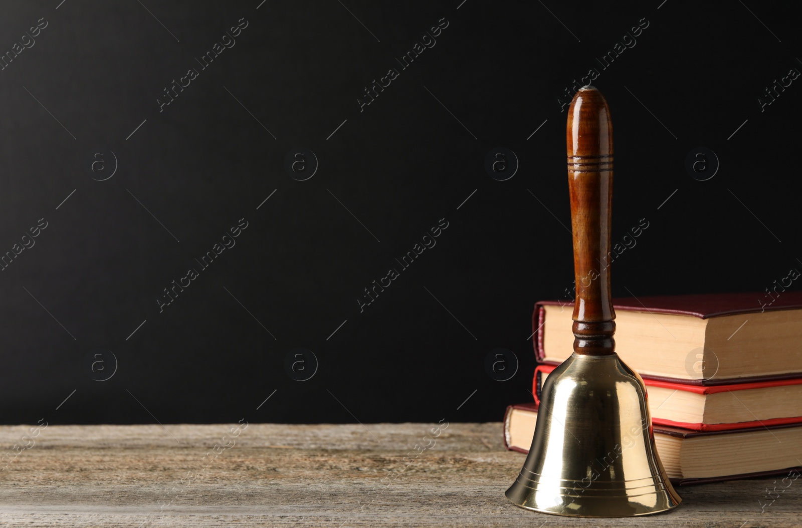 Photo of Golden bell and stack of books on wooden table near blackboard, space for text. School days